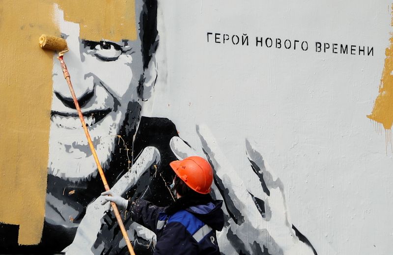 A worker paints over a graffiti depicting Alexei Navalny in