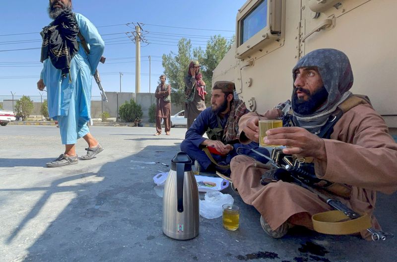 Armed Taliban men drink tea as Taliban forces block the