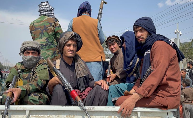 Taliban forces patrol near the entrance gate of Hamid Karzai