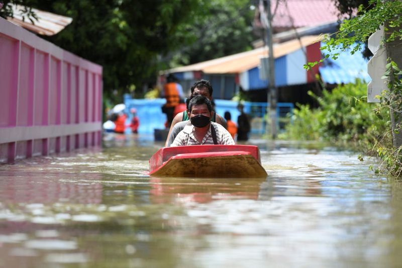 People ride a boat through a flooded street, in Thailand’s