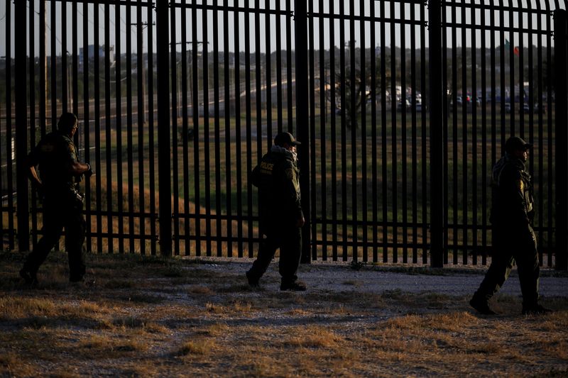 U.S. Border Patrol officers walk along the perimeter fence near