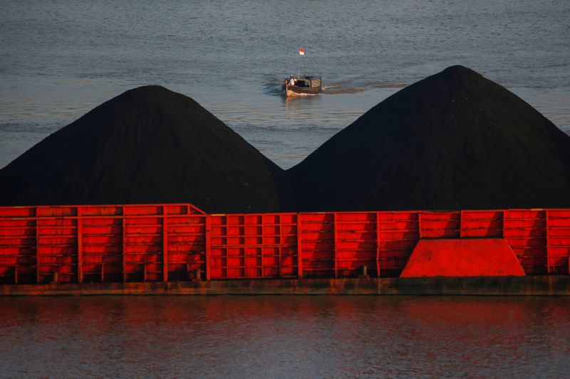Man stands on a boat as coal barges queue to