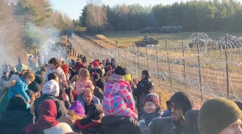 Migrants gather near a barbed wire fence on the Poland