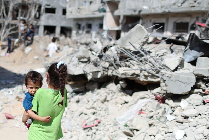 A Palestinian girl carries a boy amid the rubble of