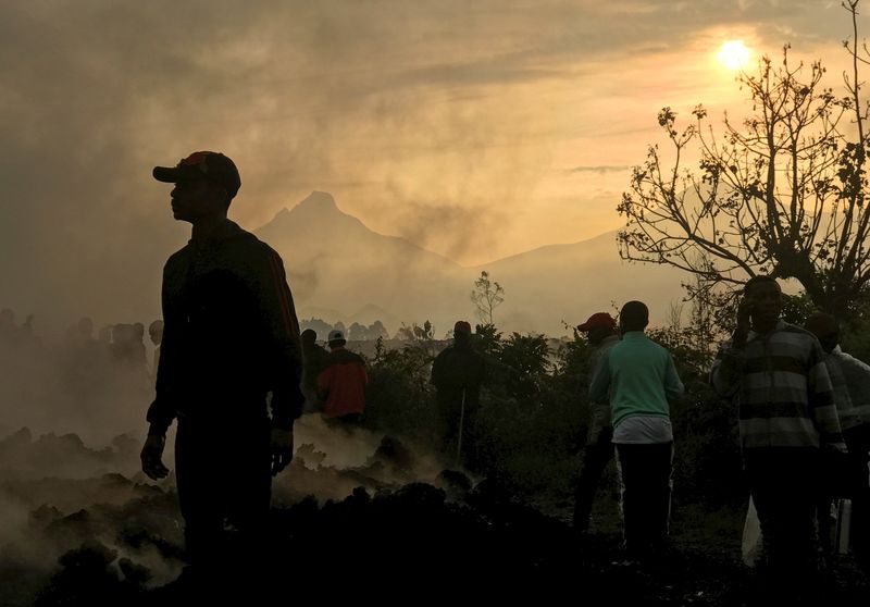 Residents walk near destroyed homes with the smouldering lava deposited
