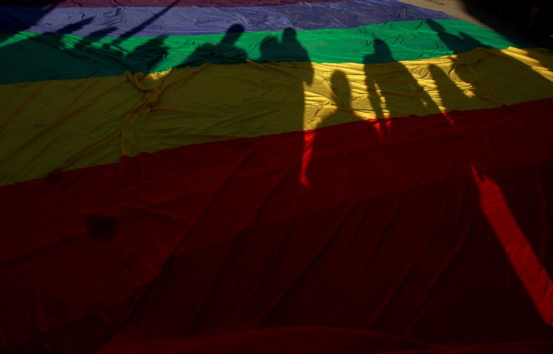 Participants’ shadows are seen on a rainbow flag during a