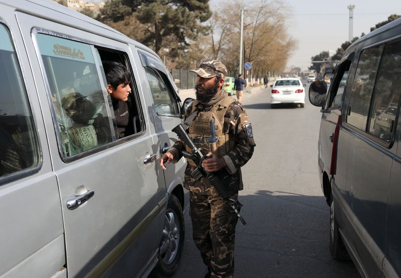 A Taliban fighter searches a car as he guards a