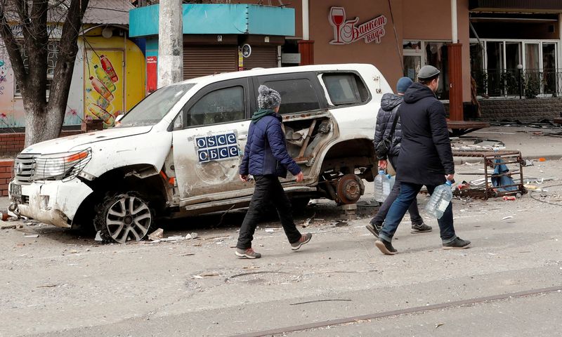 FILE PHOTO: People walk past a damaged OSCE car in