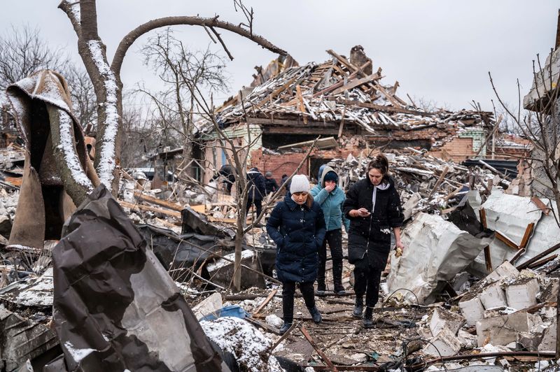 Women walk among remains of residential buildings destroyed by shelling,