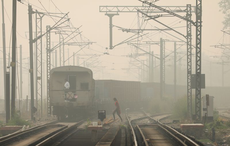 A woman crosses railway tracks as a goods train passes