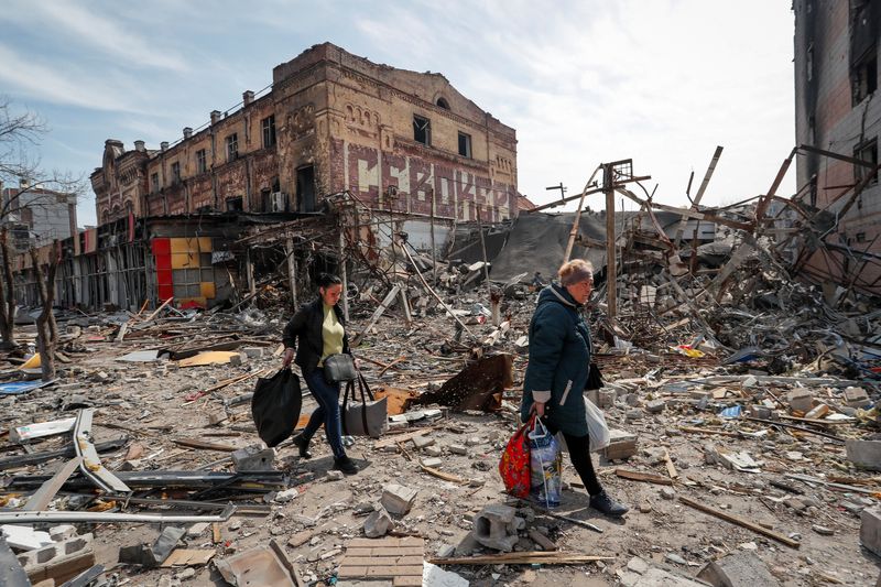 Residents carry their belongings near buildings destroyed in the course