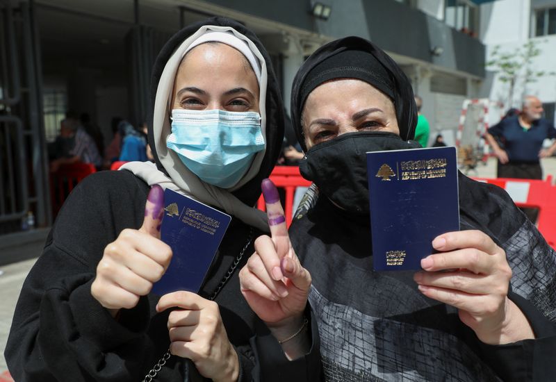 Women pose as they hold their Lebanese passports and show