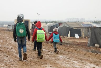 Internally displaced Syrians walk together near tents at a camp