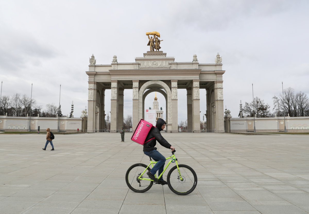 A delivery courier rides a bicycle past an entrance of