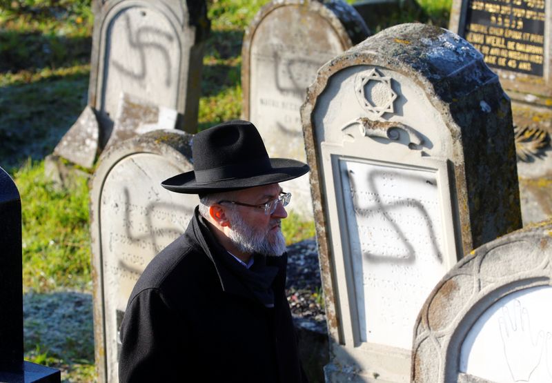 A man walks past graves desecrated with swastikas at the