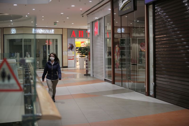 A woman wearing protective face mask walks past closed shops