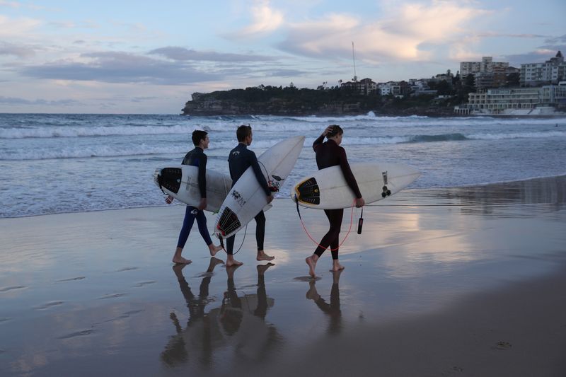 Surfers walk along the water’s edge at Bondi Beach in