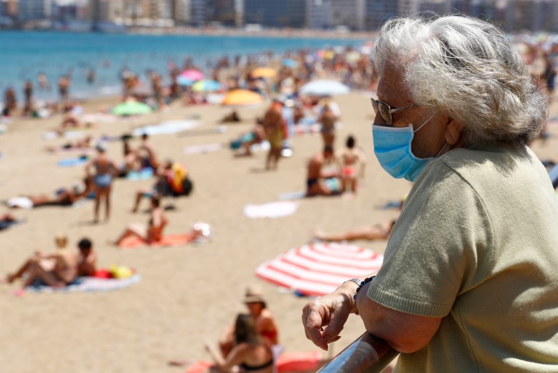 A woman wearing a face mask watches people sunbathing on