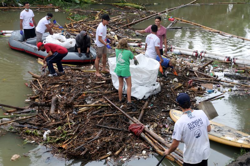 Volunteers collect trash trapped by barriers, which are called ‘trash