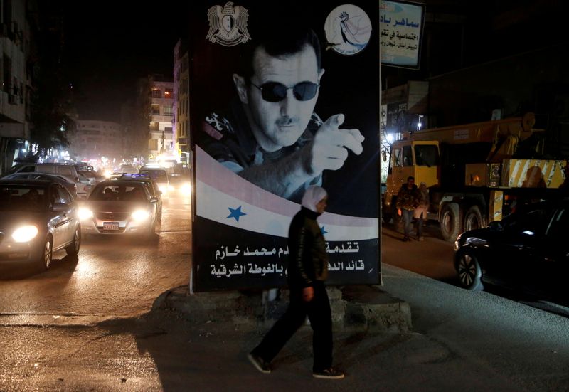 FILE PHOTO: A woman walks past a poster depicting Syria’s
