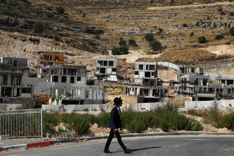 A Jewish settler walks past Israeli settlement construction sites around