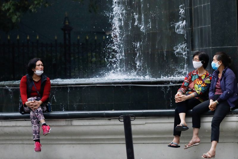 Women wear protective masks as they chat on a street