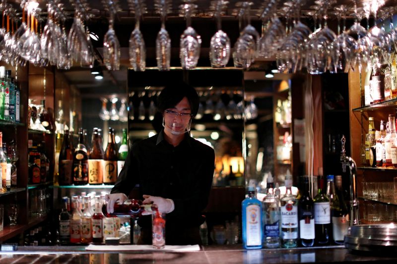 A bartender wearing a face shield makes a cocktail, amid