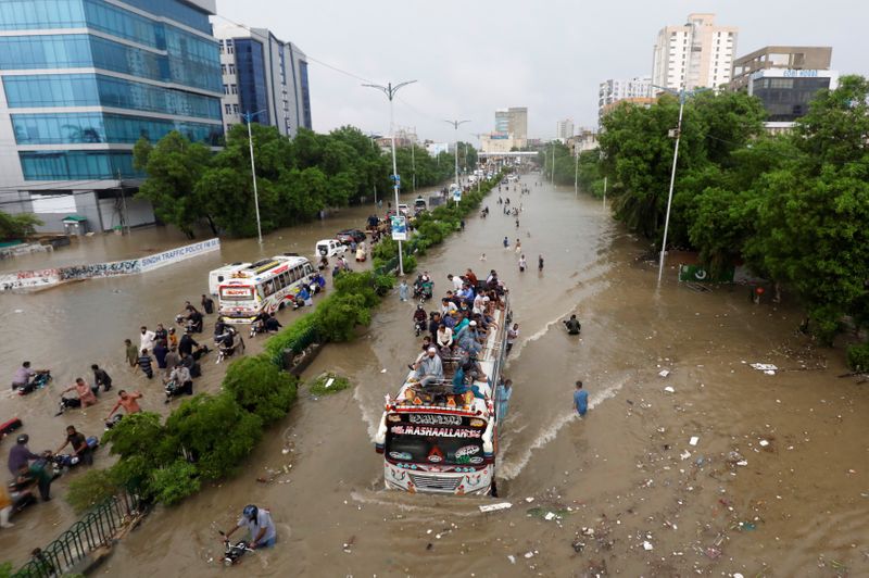 People sit atop a bus roof while others wade through