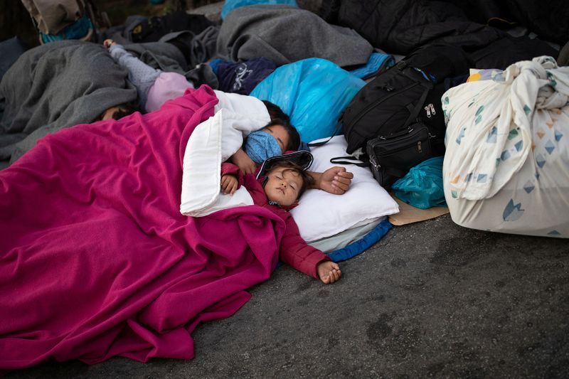 Refugees and migrants sleep on a road following a fire