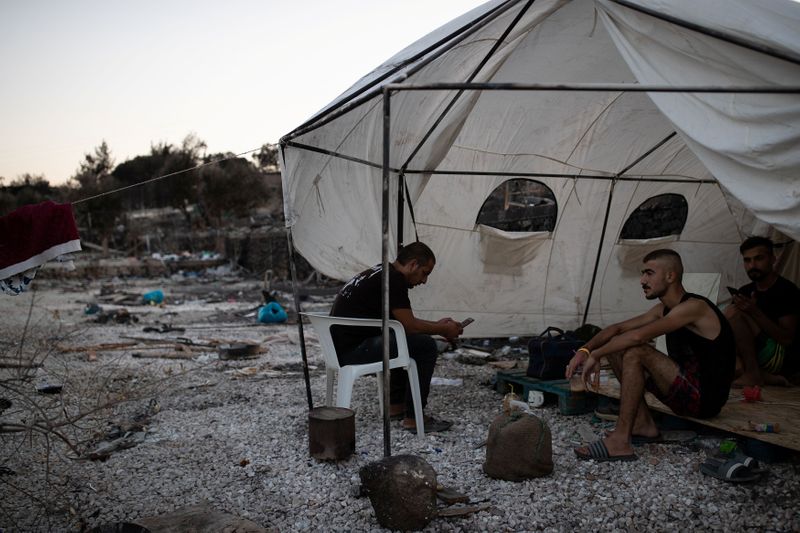 Men sit in a makeshift shelter next to burnt tents