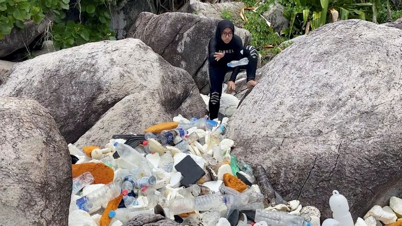 A woman clears trash by the sea at Tioman Island,