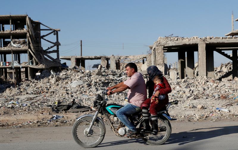 FILE PHOTO: Motorists ride a motorcycle past ruins of buildings