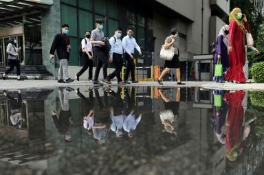 People wearing protective masks are reflected in a water puddle
