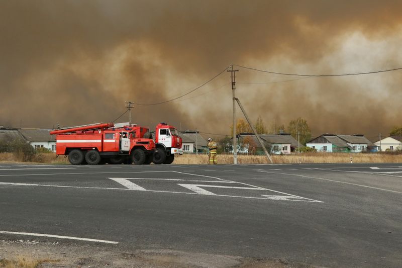 Fire trucks are seen on the road as smoke rises