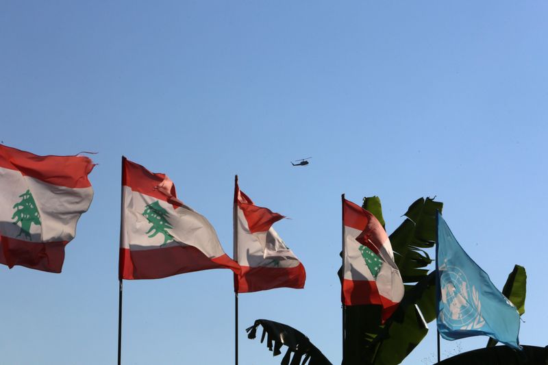 Lebanese and UN flags flutter as an aircraft flies in