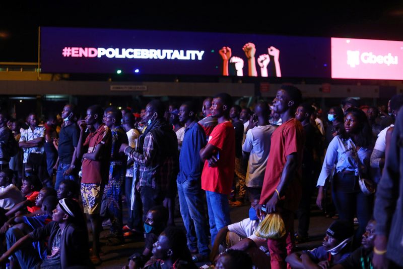 Demonstrators gather beside an electronic billboard displaying the slogan “End