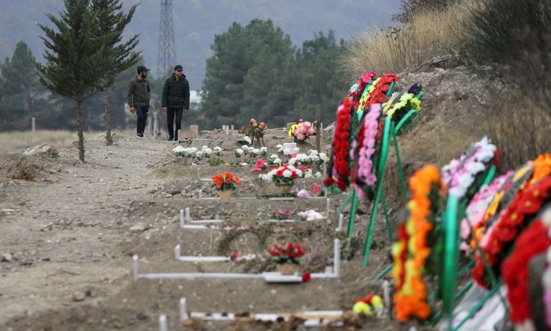 Men walk along graves of soldiers and civilians who were