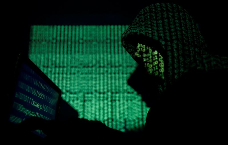 FILE PHOTO: Hooded man holds a laptop computer as cyber