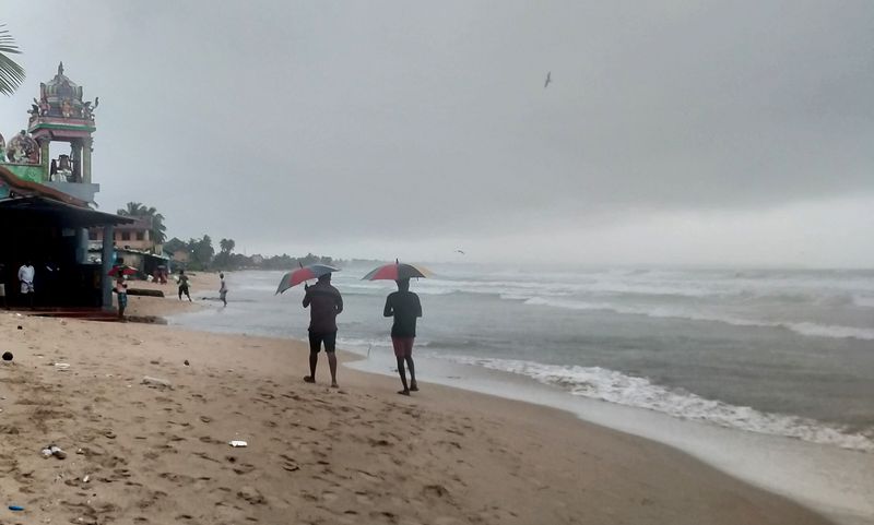 Two men walk along a beach as Cyclone Burevi is