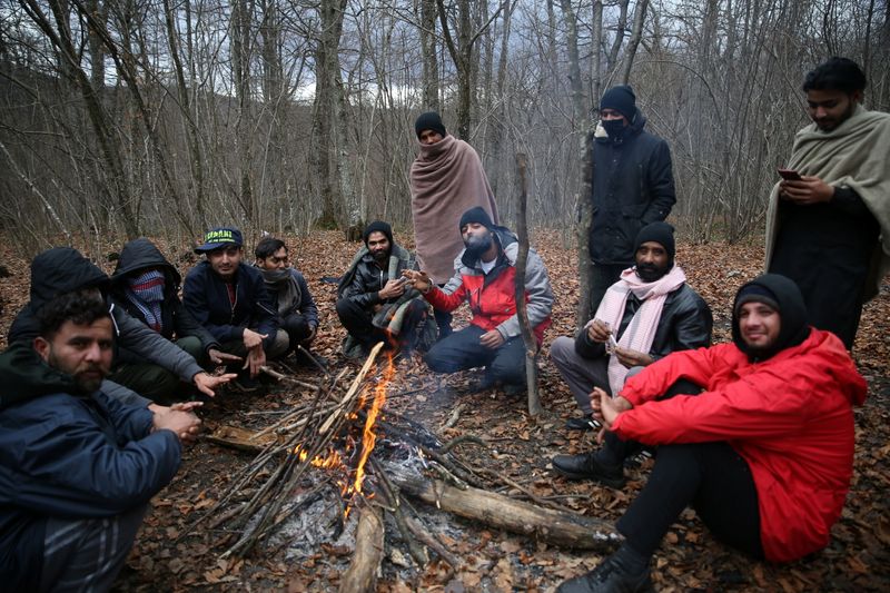 Migrants try to warm themselves near the burned migrant center