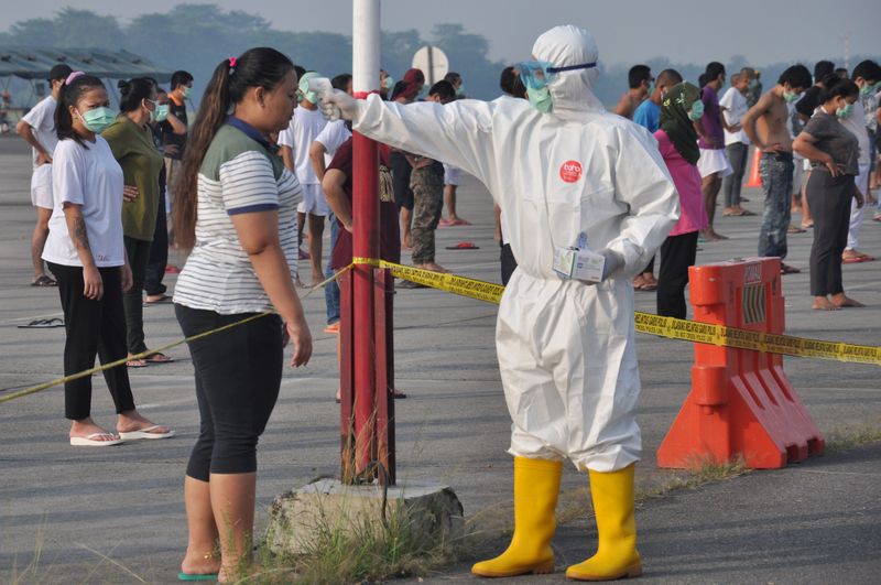 Officer wearing protective gear checks temperature of Indonesian migrant worker