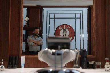 Angelos Antonopoulos, is reflected in a mirror in his barbershop