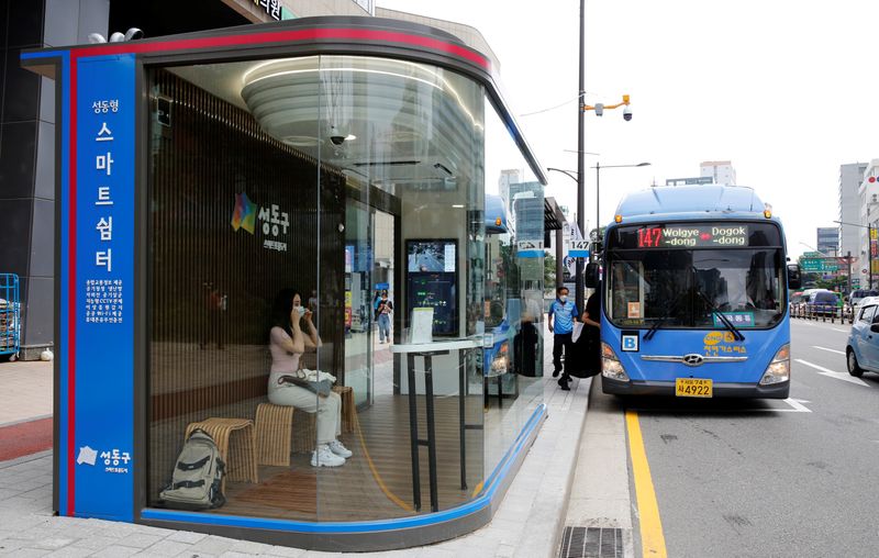 Woman waits for a bus inside a glass-covered bus stop