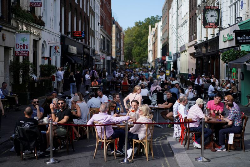 People sit at the tables outside restaurants in Soho, amid