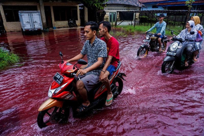 People ride motorbikes through a flooded road in Pekalongan