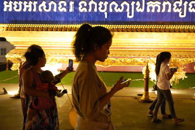 People walk using their mobiles phones in Phnom Penh
