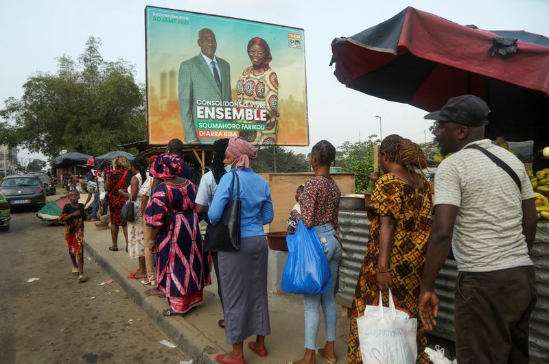 People stand in line under a campaign billboard showing the