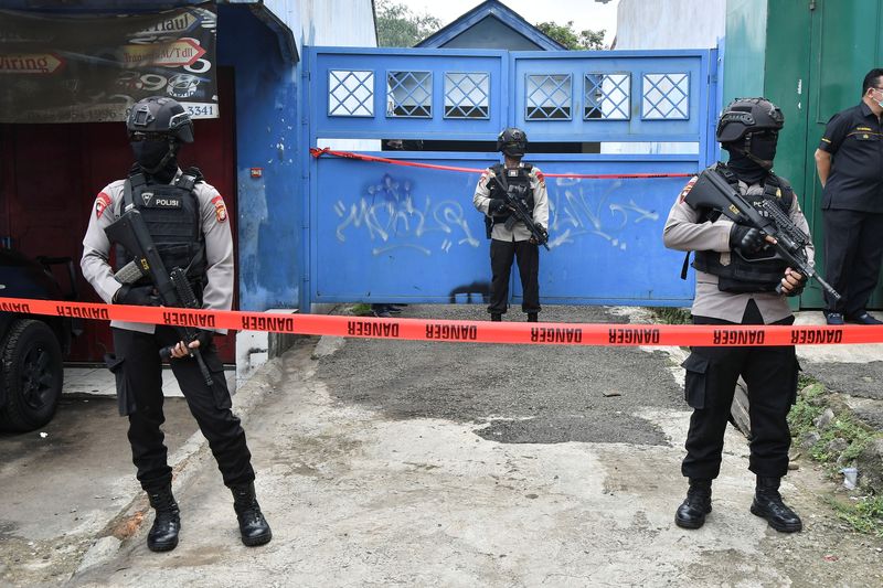 Armed police officers stand guard outside a house during a