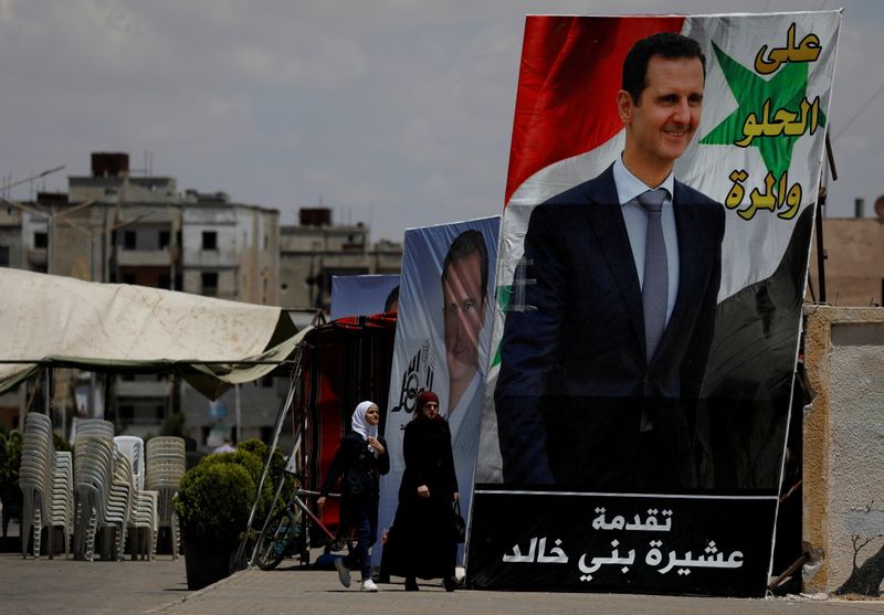 FILE PHOTO: People walk past posters depciting Syria’s President Bashar