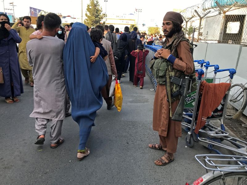 A member of Taliban stands guard as people walk at